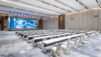 A conference room with rows of tables and chairs, a large screen, and a modern ceiling design.