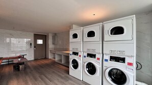 A laundry room with four stacked front-loading washing machines, a bench, and a small table with a potted plant. - EVEN Hotel Shenzhen Guangming Cloud Park by IHG (Shenzhen)