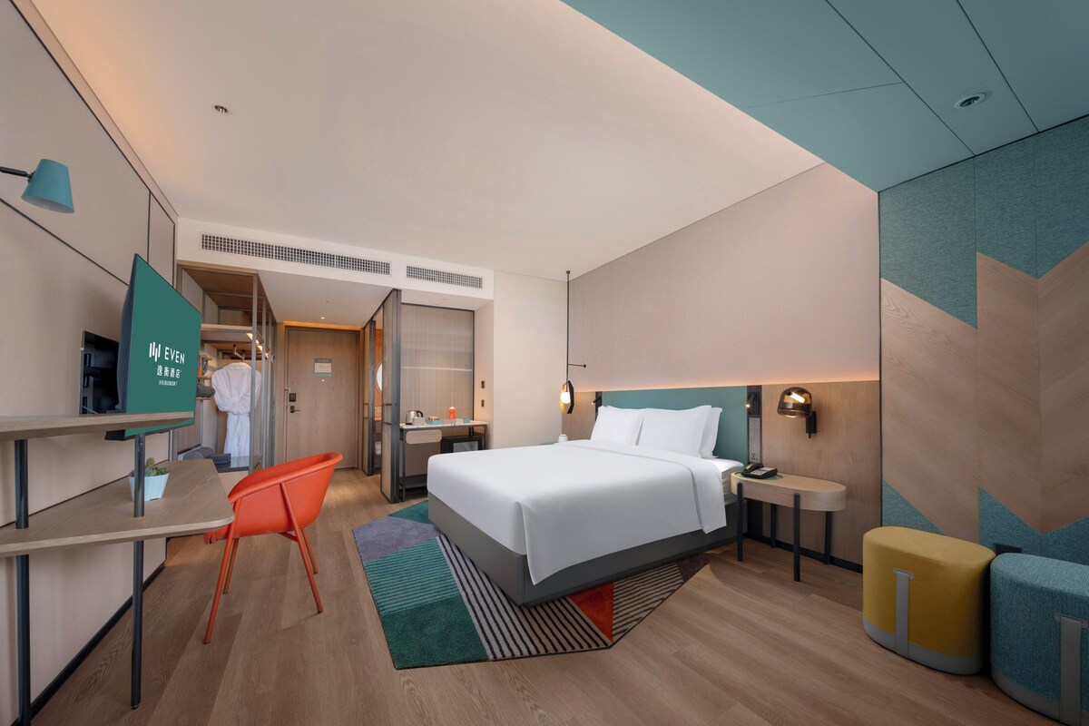 Una habitación de hotel moderna con cama, escritorio, silla y un baño visible a través de una puerta abierta.