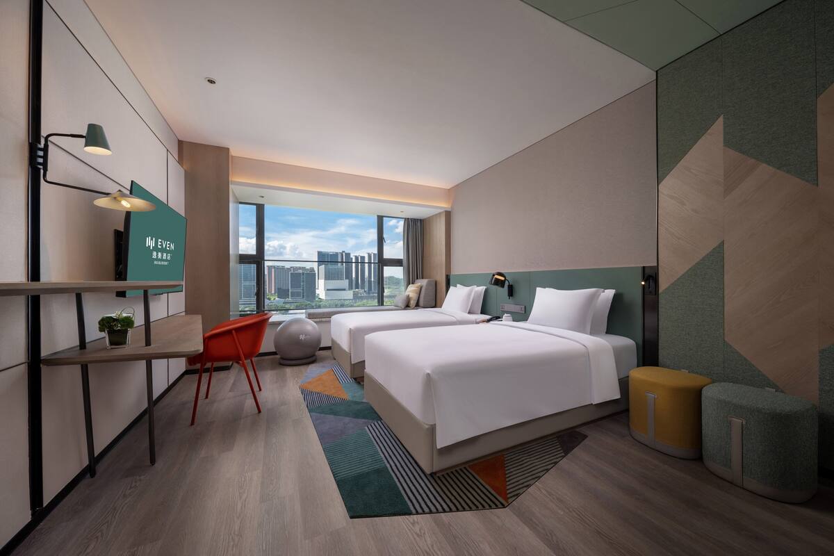 A modern hotel room with a large bed, a desk, and a view of the city.
