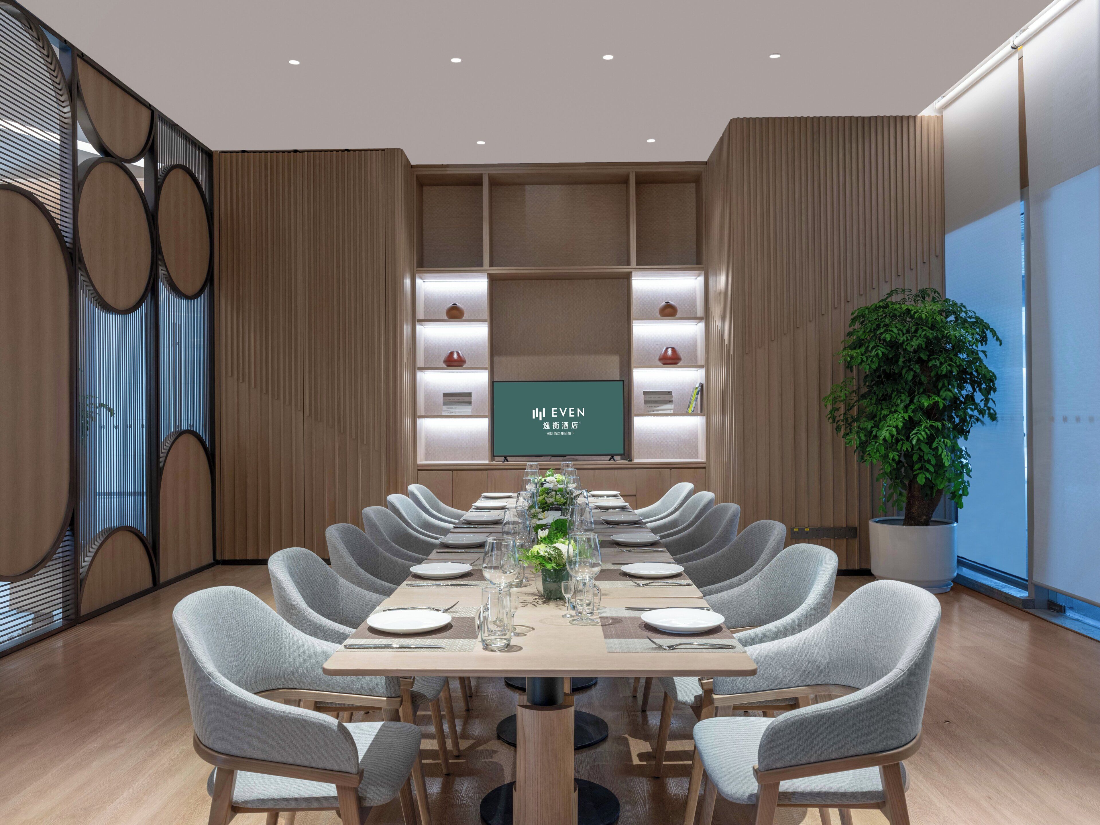 A conference room with a long table, chairs, a television screen, and shelves with decorative items.