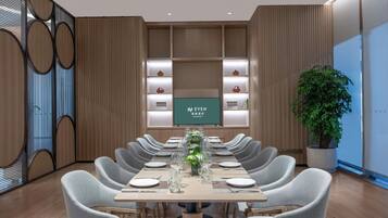 A conference room with a long table, chairs, a television screen, and shelves with decorative items.
