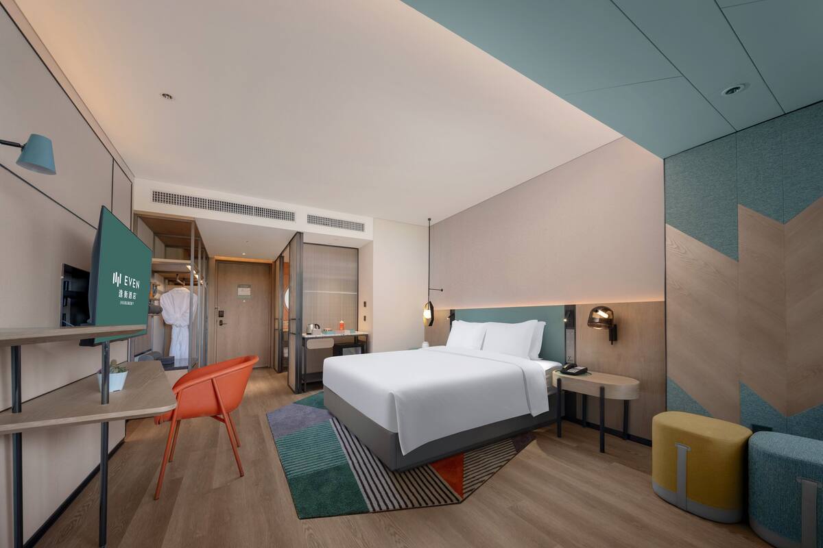 A modern hotel room with a bed, desk, chair, and a bathroom visible through an open door.