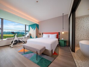 Een moderne hotelkamer met een groot bed, een trainingsfiets, uitzicht op de bergen en een groot raam.