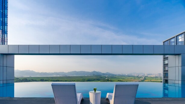 A rooftop infinity pool with two white wicker lounge chairs and a small table with a vase, overlooking a scenic landscape with mountains and a bridge. - EVEN Hotel Shenzhen Guangming Cloud Park by IHG (Shenzhen)
