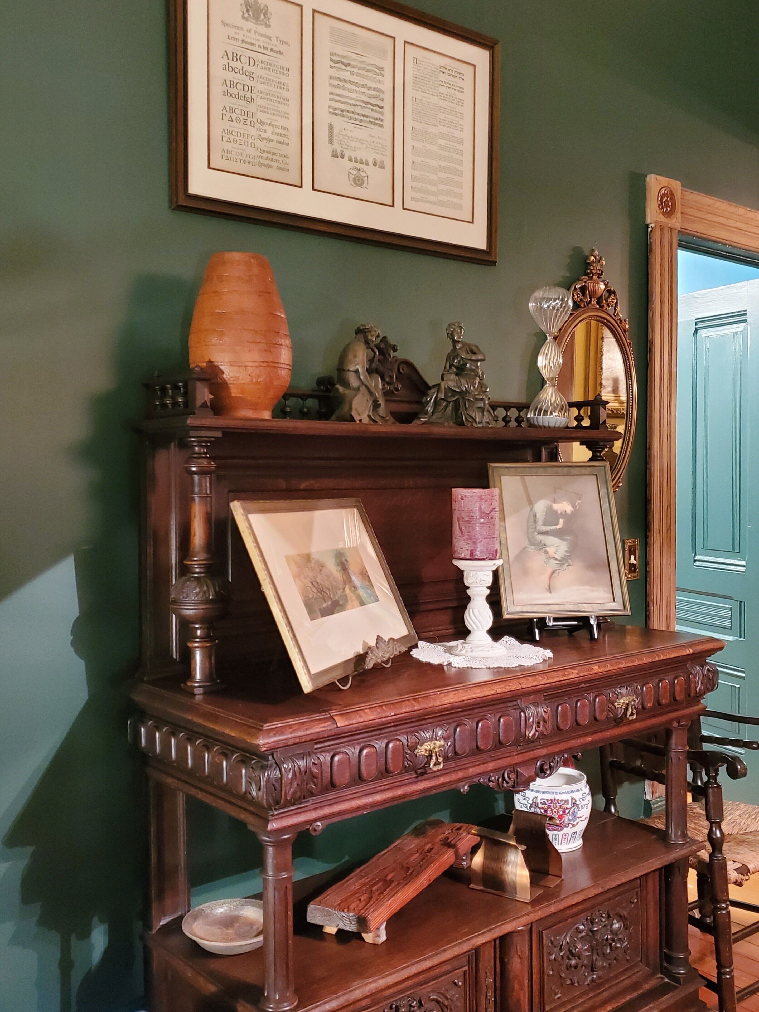 Een houten dressoir met een spiegel, ingelijste documenten en decoratieve objecten.