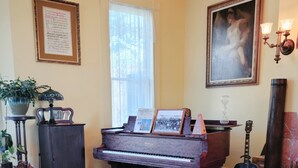 A living room with a grand piano, a sofa, a rug, a guitar, and a painting on the wall. - The Adams Pragge House (Port Townsend)