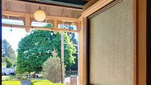 A room with a large window, a door with a handle, and a view of a garden with hedges and a tree. - The Adams Pragge House (Port Townsend)