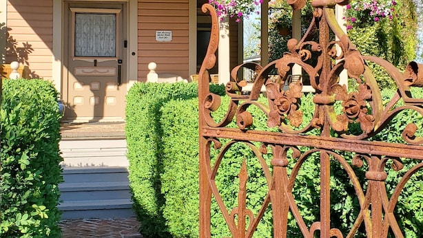 A wooden house with a decorative iron gate, a well-maintained hedge, and a clear pathway leading to the entrance. - The Adams Pragge House (Port Townsend)