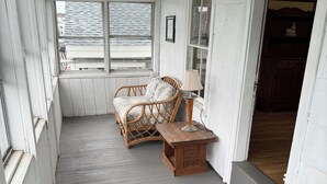 Eine überdachte Veranda mit einem Korbsessel und einem Holztisch mit einer Lampe.