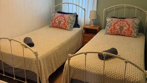 Ein Zimmer mit zwei Einzelbetten, einem Nachttisch mit Lampe, einem Fenster mit Vorhängen und einer Klimaanlage an der Wand.