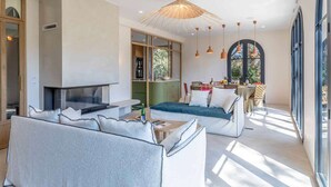 A modern living room with a fireplace, a dining area, and large windows offering a view of the outdoors.