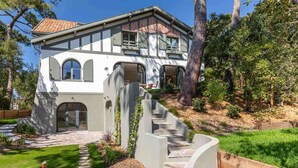 A two-story house with a stone staircase leading to the entrance, surrounded by a well-maintained garden and trees.