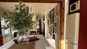 Una cocina con encimera blanca, un florero de vidrio con hojas verdes, una tabla de cortar de madera y un refrigerador blanco.