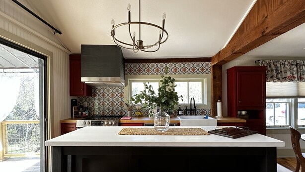 Una cocina moderna con una isla grande, taburetes de madera, una araña y vistas al exterior.