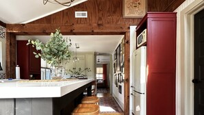 Una cocina con techo de madera, una isla blanca con taburetes y un refrigerador rojo.