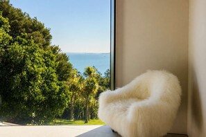 Una habitación con un ventanal grande que da a un paisaje verde y exuberante y al mar.