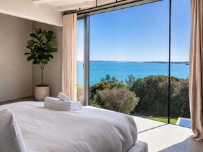 Ein Schlafzimmer mit einem großen Bett, einer Zimmerpflanze und Blick auf das Meer.