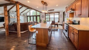 A spacious kitchen with a large island, wooden beams, and a stone fireplace. - R&R White Mountain Retreat, Hillside with Extraordinary Views! (Fryeburg)
