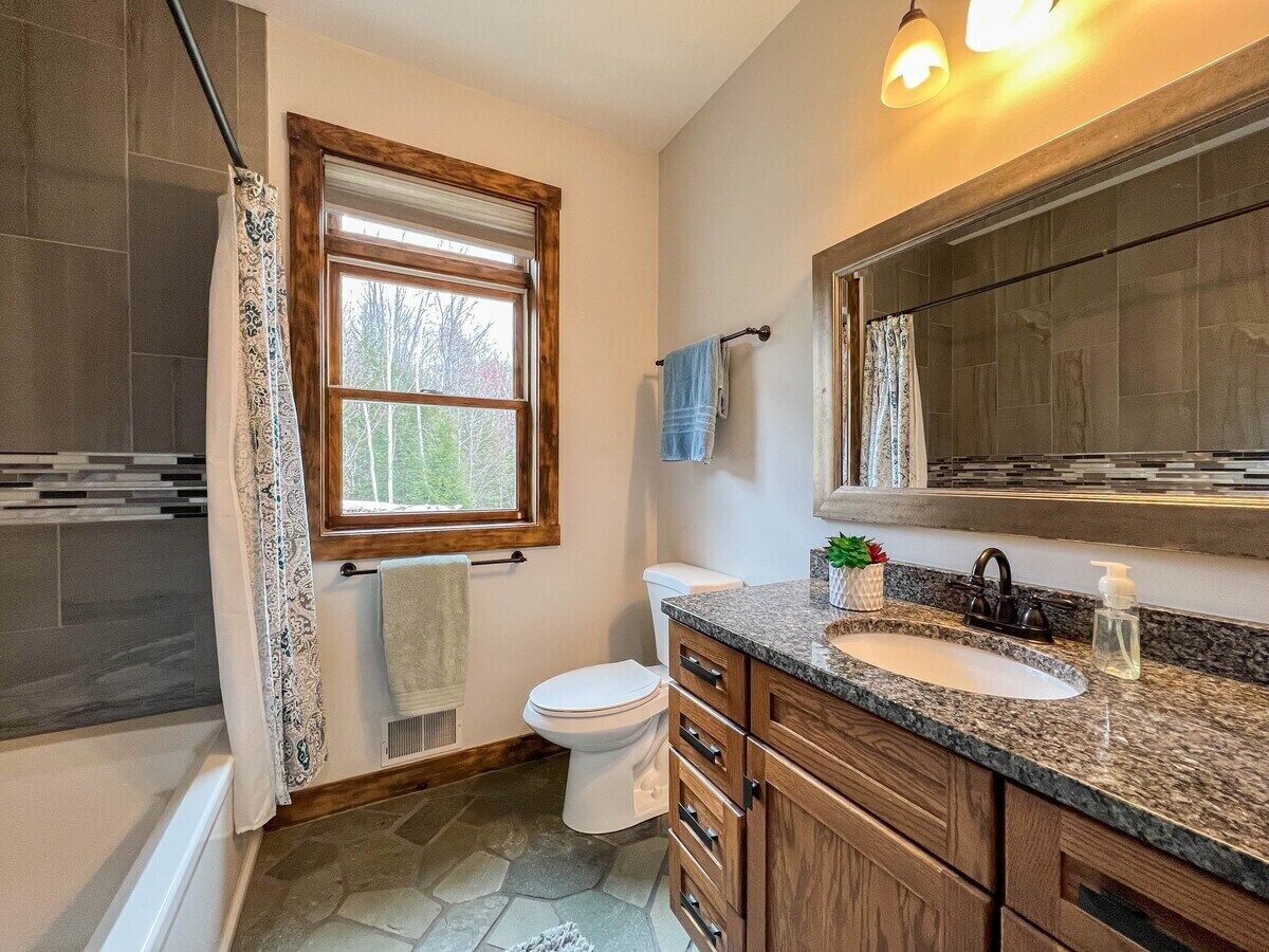 A bathroom with a window, a toilet, a sink, and wooden cabinets.