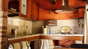 A kitchen with a brick wall, wooden cabinets, a marble countertop, and a hanging pot rack. - Panoramic Sea Views Immersed in Nature Quiet Peaceful Private Villa Retreat (Toscana)