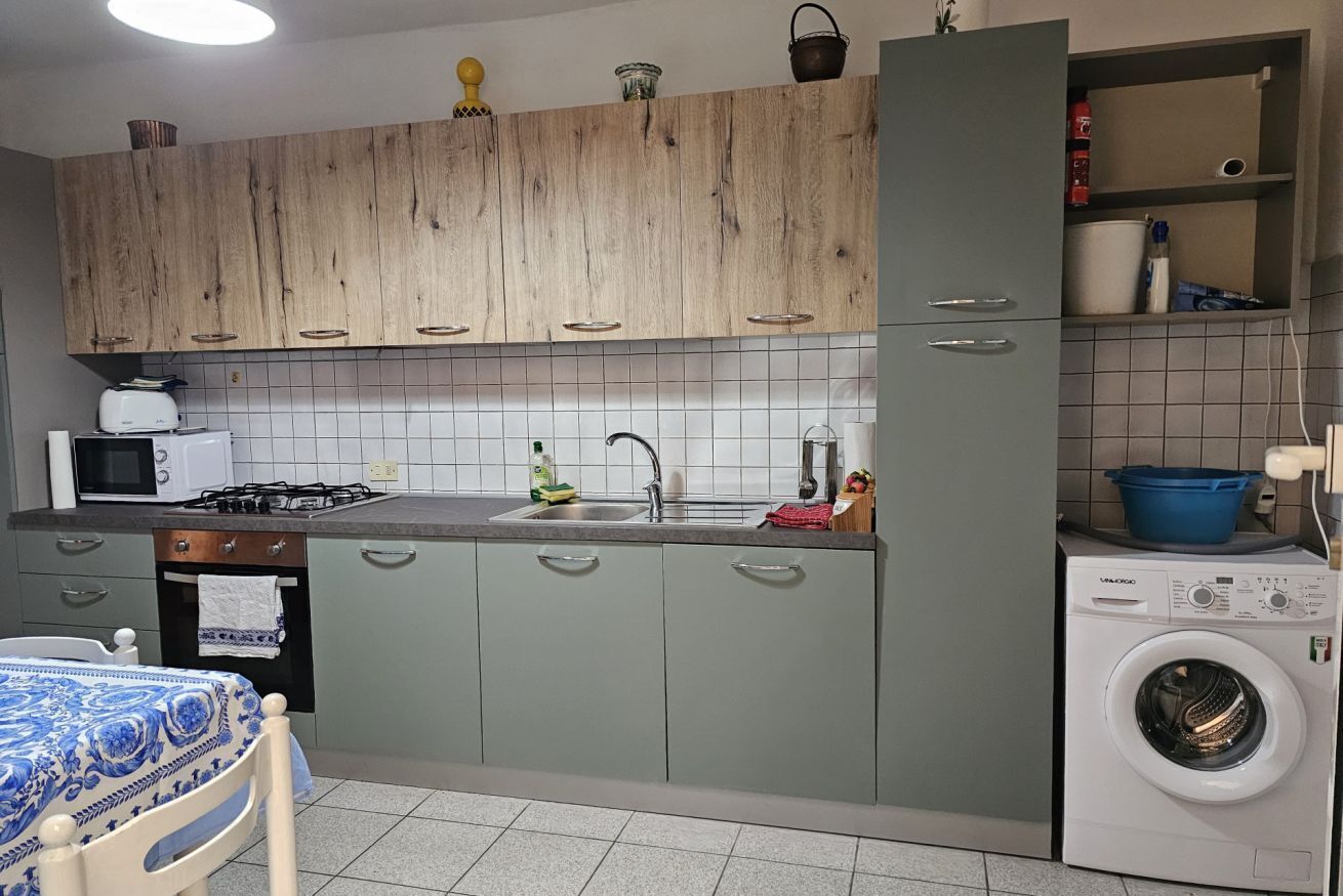 A kitchen with wooden cabinets, a washing machine, a sink, and a table with a blue tablecloth.