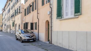 A car parked on a street next to a building with green shutters and a beige facade.