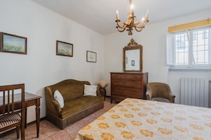 Una camera da letto con un letto, una cassettiera in legno, un divano marrone, una sedia di legno e un lampadario.