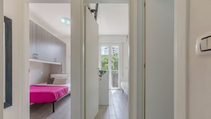 Un couloir étroit mène à une chambre à coucher où se trouve un lit recouvert d’une couverture rose.
