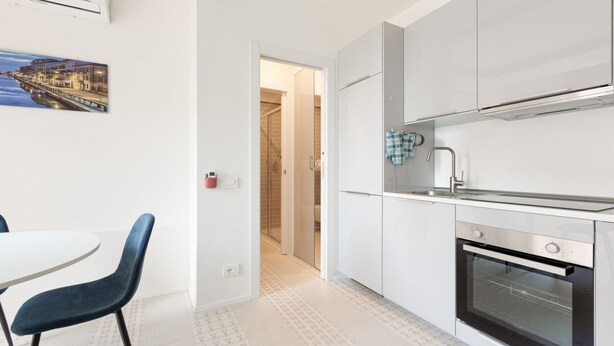 A modern kitchen with white cabinets, a built-in oven, and a dining area with a table and chairs. - GuestHost - Renovated studio apartment with all amenities! (Milano)
