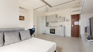 A modern hotel room with a bed, a desk, a kitchenette, and a TV. - GuestHost - Renovated studio apartment with all amenities! (Milano)
