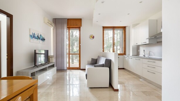 A modern kitchen with white cabinets, a built-in oven, and a dining area with a wooden table and chairs.
