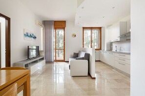 A modern kitchen with white cabinets, a built-in oven, and a dining area with a wooden table and chairs.