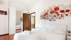 A hotel room with a large bed, a wardrobe, a mirror, and a painting of red flowers on the wall.