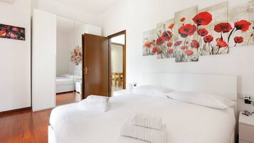 Ein Hotelzimmer mit einem großen Bett, einem Schrank, einem Spiegel und einem Gemälde mit roten Blumen an der Wand.