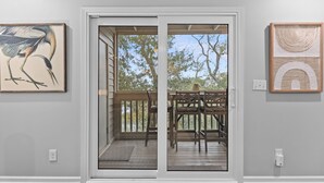 A room with a sliding glass door leading to an outdoor deck with a wooden railing and chairs. - 2 BR/2BA w/Stunning Marsh Views! Amenity access included! (Seabrook Island)