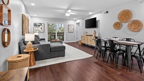 A modern living room with a grey sofa, wooden side tables, and a dining area with a table and chairs. - 2 BR/2BA w/Stunning Marsh Views! Amenity access included! (Seabrook Island)