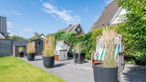 A courtyard with potted plants, outdoor furniture, and a pathway leading to a house. - Modern. Ruhig. Wiesenblick. - Ringhoog Hüs Whg. 5 "weitblick" - Objekt-id: Rhh/05 - Ringhoog Hüs (Sylt)