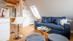 A modern loft apartment with a dining area, a blue sofa, and a glass coffee table. - Modern. Ruhig. Wiesenblick. - Ringhoog Hüs Whg. 5 "weitblick" - Objekt-id: Rhh/05 - Ringhoog Hüs (Sylt)