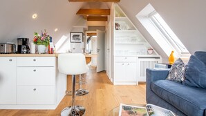 A modern loft apartment with a kitchen, dining area, and living room. It features a skylight, wooden beams, and a cozy seating area. - Modern. Ruhig. Wiesenblick. - Ringhoog Hüs Whg. 5 "weitblick" - Objekt-id: Rhh/05 - Ringhoog Hüs (Sylt)
