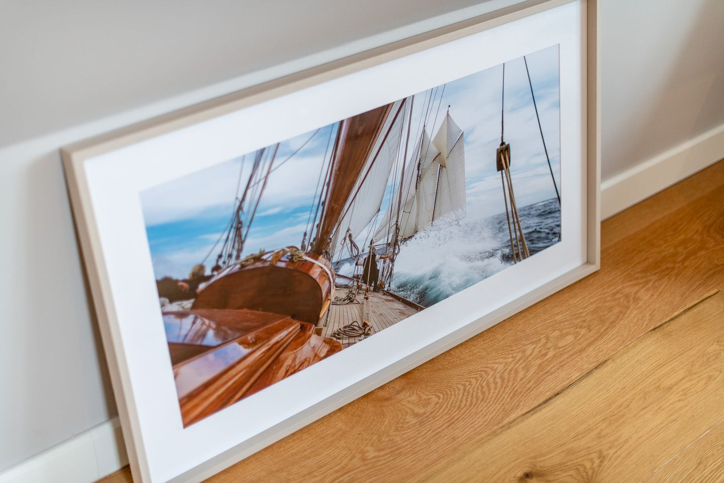 A framed photograph of a sailing ship on the sea, mounted on a wooden floor.