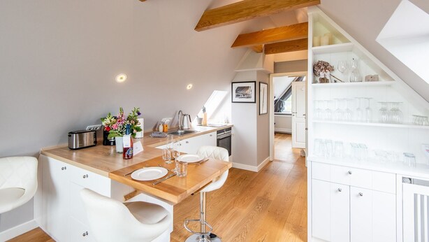 A modern kitchen with a wooden countertop, white cabinetry, and a dining area with white chairs. - Modern. Ruhig. Wiesenblick. - Ringhoog Hüs Whg. 5 "weitblick" - Objekt-id: Rhh/05 - Ringhoog Hüs (Sylt)