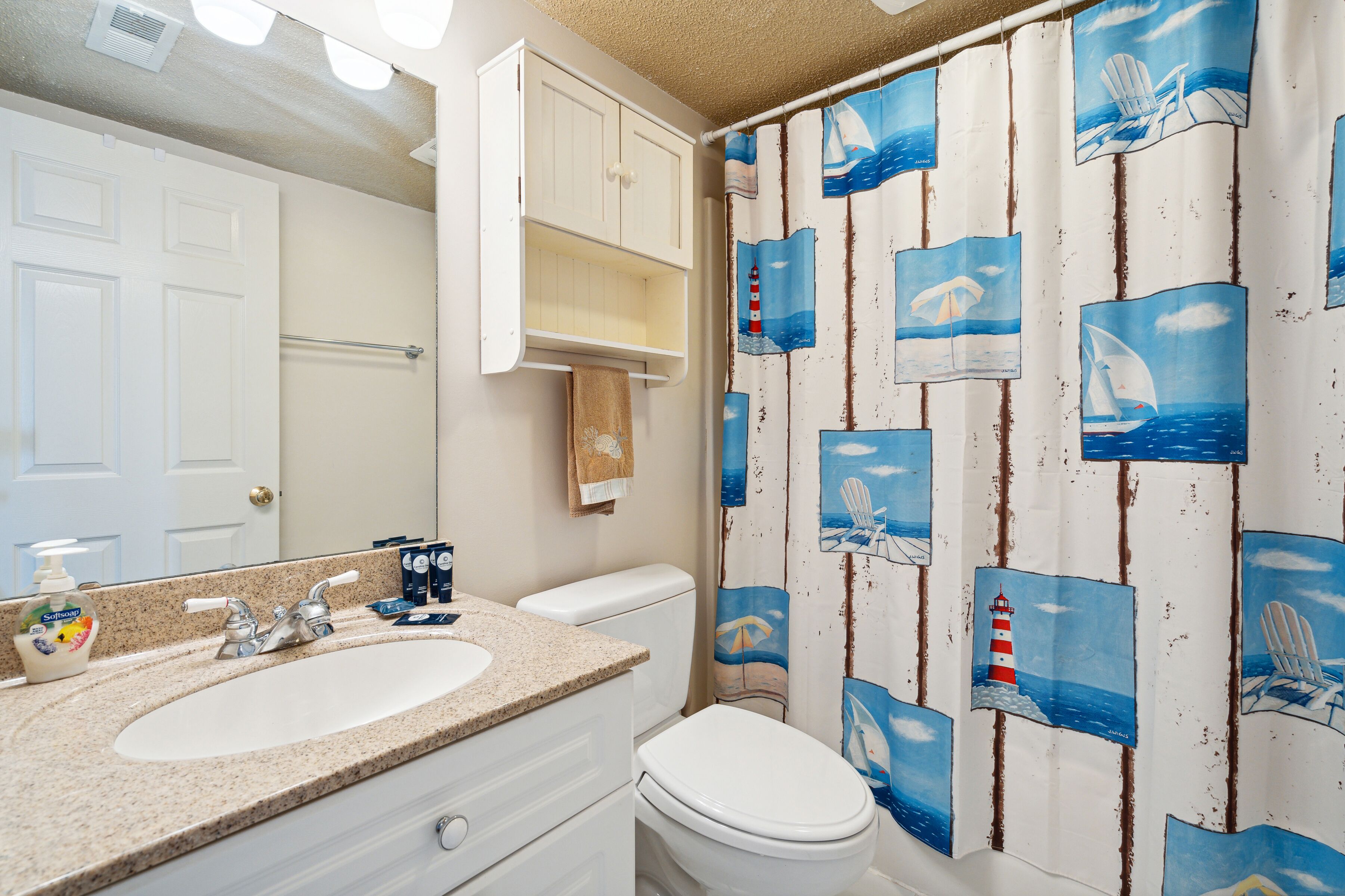 Une salle de bain avec un lavabo blanc, des toilettes et un rideau de douche orné de motifs marins.