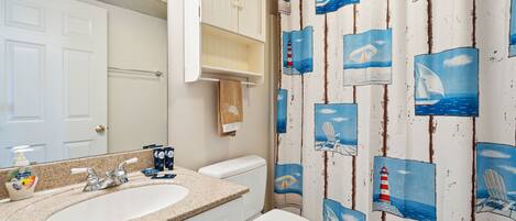 Une salle de bain avec un lavabo blanc, des toilettes et un rideau de douche orné de motifs marins.