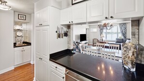 A kitchen with white cabinets, a black countertop, and a dining area with a white table and chairs.