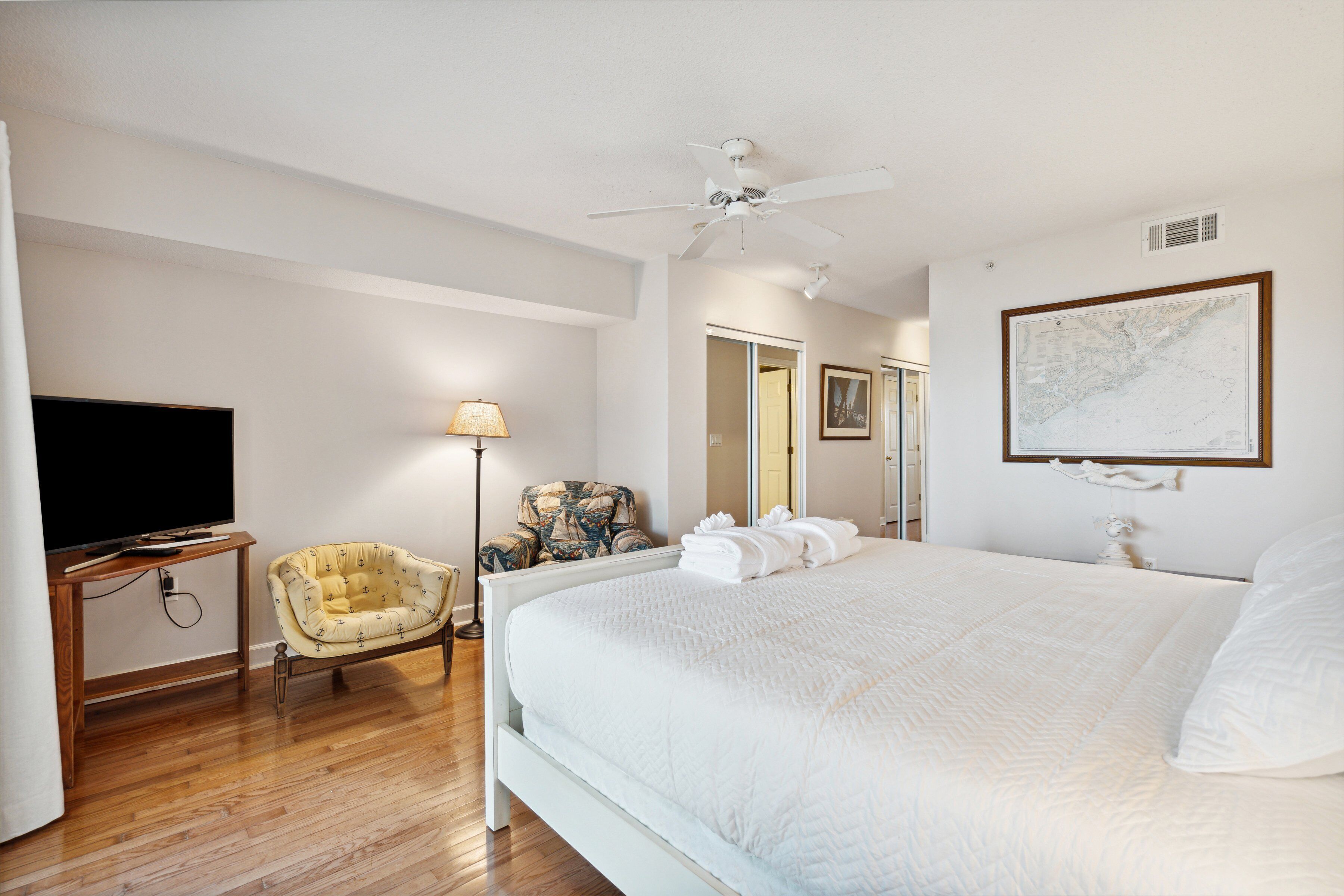 A hotel room with a large bed, a television, a chair, and a ceiling fan.