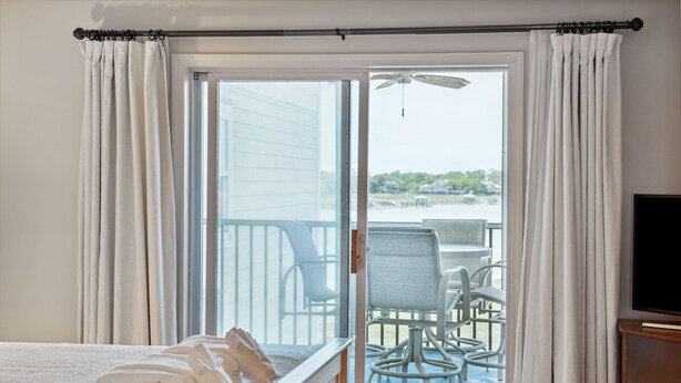 A hotel room with a bed, a balcony with chairs, and a view of the water.