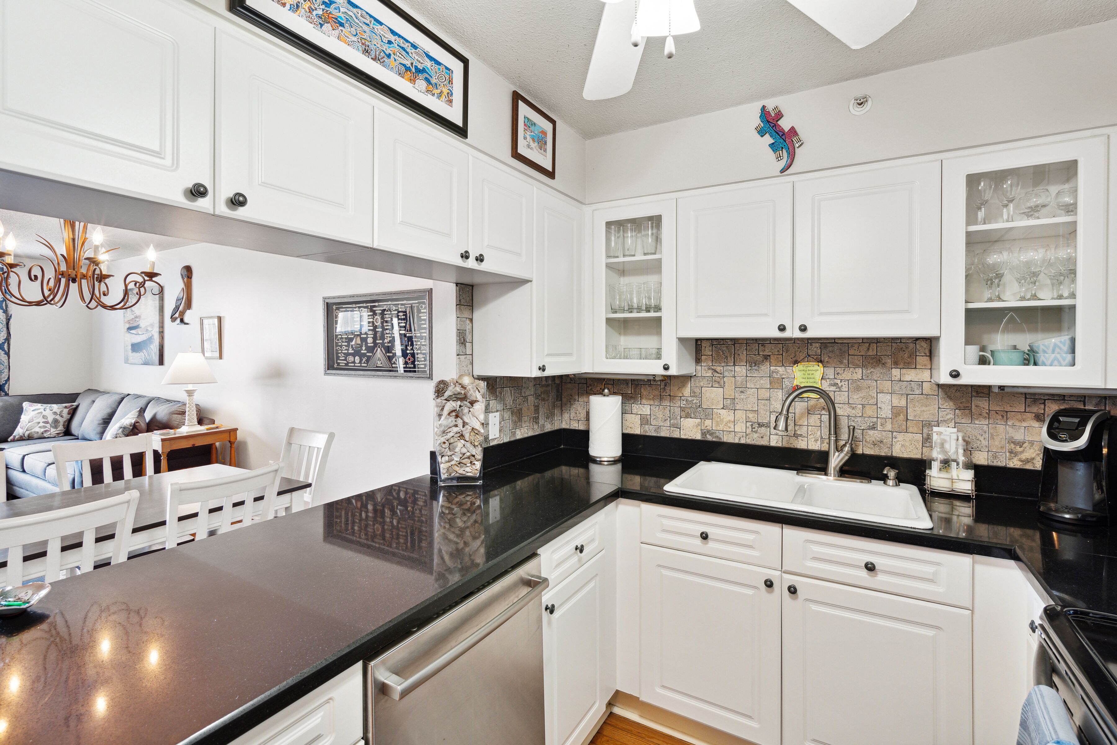 A modern kitchen with white cabinetry, a black countertop, and a built-in dishwasher.