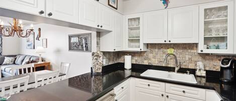 A modern kitchen with white cabinetry, a black countertop, and a built-in dishwasher.