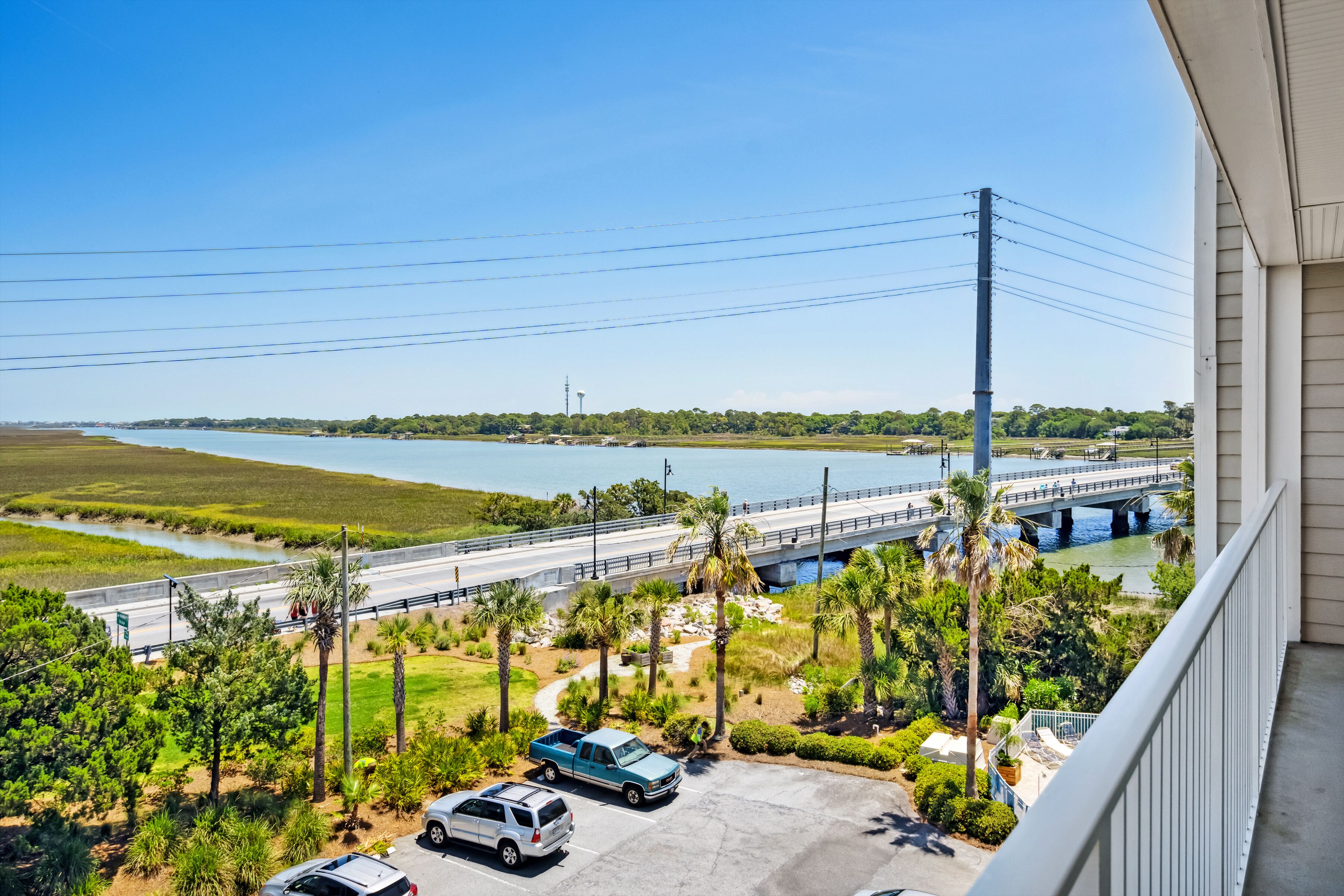 Vista desde un balcón sobre un estacionamiento con un puente sobre un río, rodeado de vegetación y palmeras.